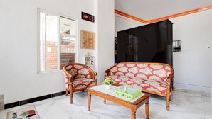 A living room with a sofa, two armchairs, a coffee table, and a small table with bottles. There is a window, a door, and a wall clock. - Hotel O Khayla Homestay Syariah (Giripurwo)