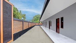 A corridor with a brick wall on one side and a plain wall on the other, leading to a set of doors. - Hotel O Khayla Homestay Syariah (Giripurwo)