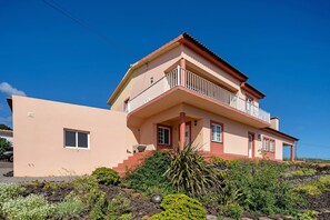 Un edificio de dos pisos con un balcón, una ventana pequeña y un camino de piedra que lleva a la entrada.