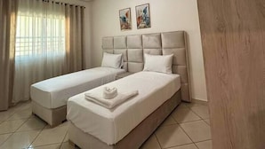 Una camera d'albergo con due letti singoli, un'ampia finestra con tende e una porta in legno.