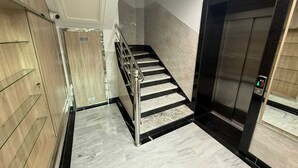 Un ascensore moderno con display digitale, una scala in marmo con ringhiere in metallo e un rivestimento murale in legno.