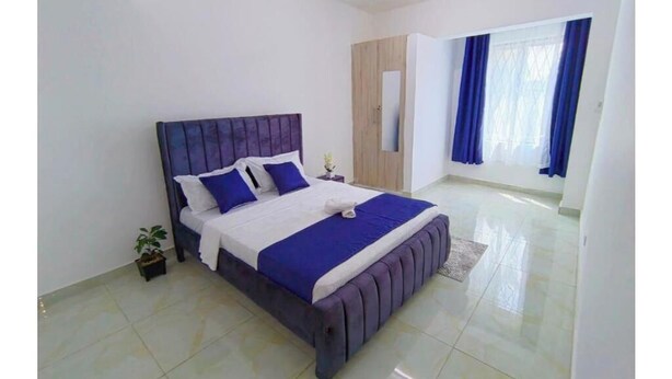 A modern bedroom with a large bed, a ceiling fan, a wardrobe, and a window with curtains.