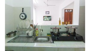 A kitchen with a sink, stove, and hanging utensils. There is a television on the wall and a door in the background.