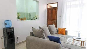 A living room with a grey sofa, a small table, a water dispenser, and a mirror on the wall.