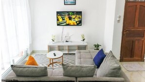 A living room with a sofa, a coffee table, a TV mounted on the wall, and a wooden door.