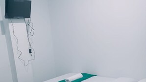 A single bed with white bedding and a green accent, a flat-screen TV mounted on the wall, and a power outlet with a cable. - Hotel O Surau Guest House (Medan)