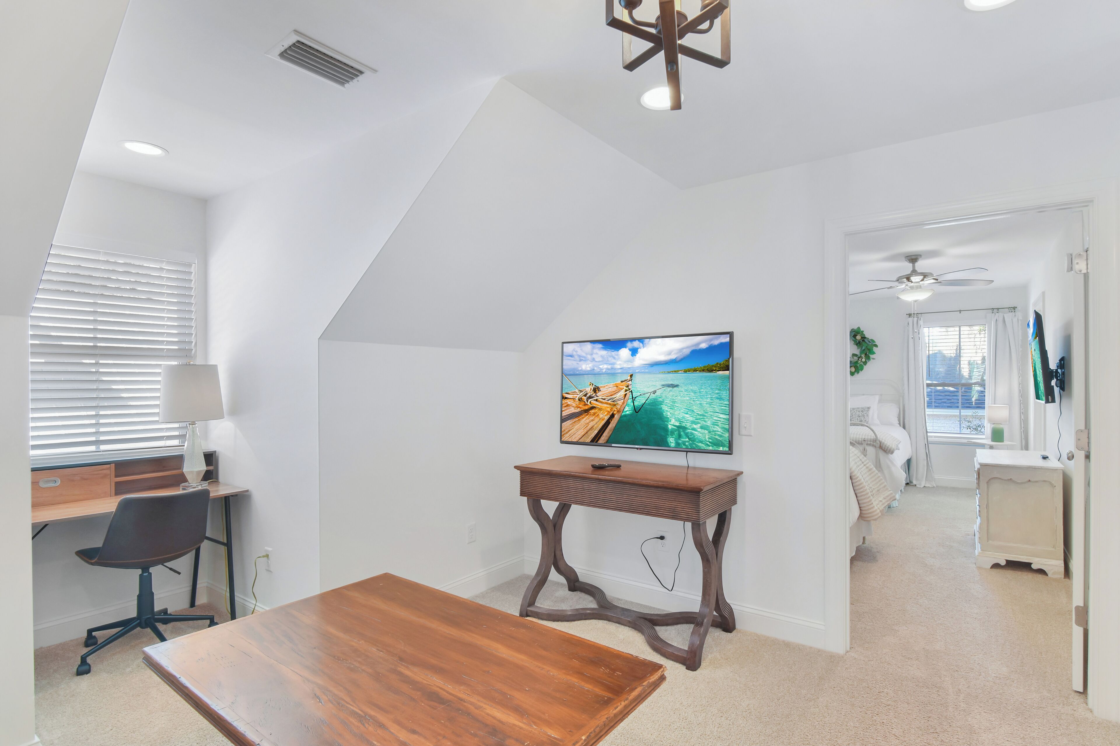 Une pièce comprenant un bureau en bois, une chaise, un téléviseur posé sur un meuble et un lit donnant sur l’extérieur.