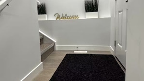 A modern interior with a staircase, a welcome sign, and decorative plants.