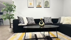 A modern living room with a black sofa, patterned cushions, a round coffee table, and a potted plant.