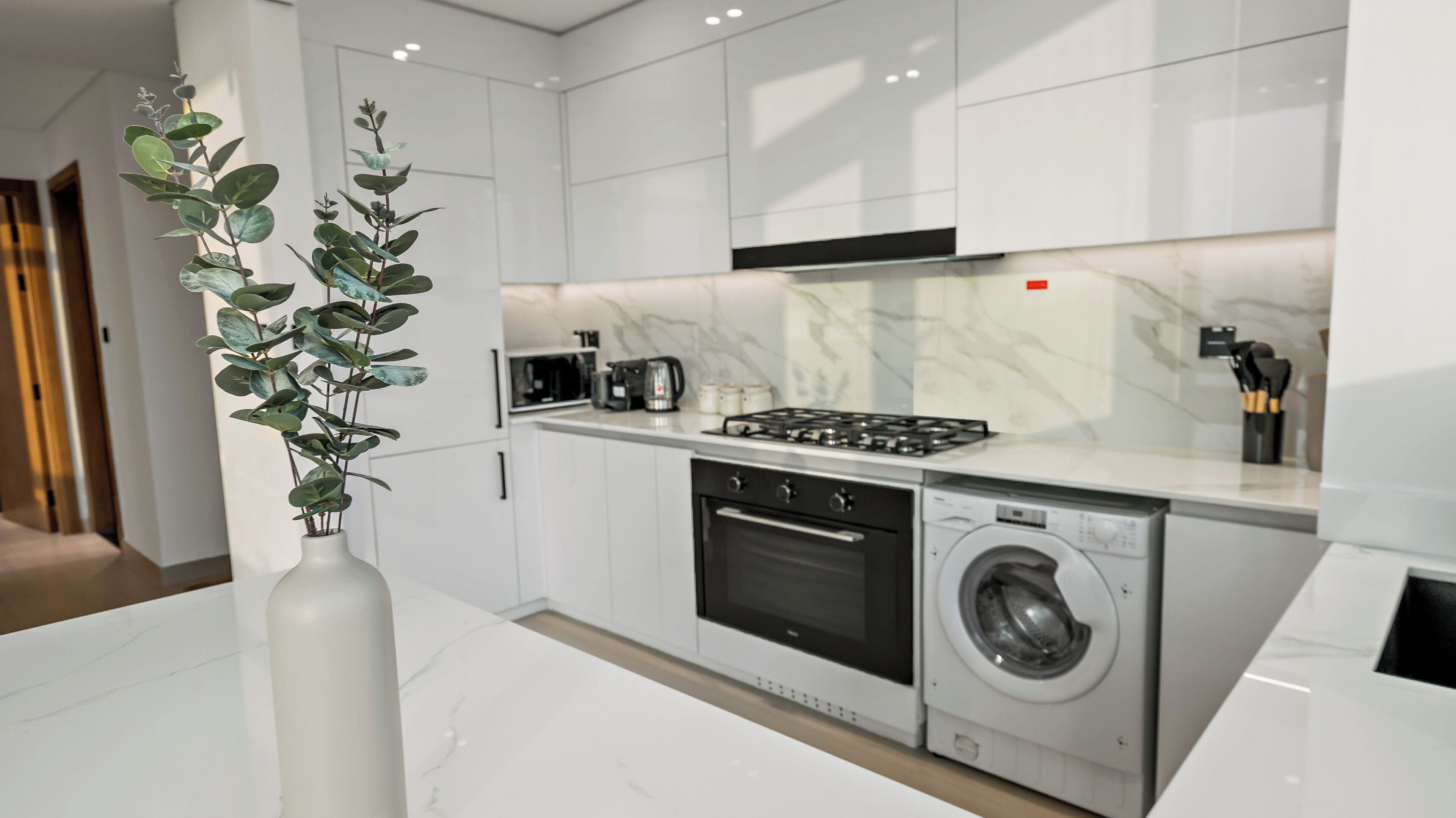 Cocina moderna con armarios blancos, estufa a gas, horno empotrado y lavadora de carga frontal.