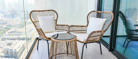 A balcony with wicker furniture and a glass table, overlooking a cityscape.