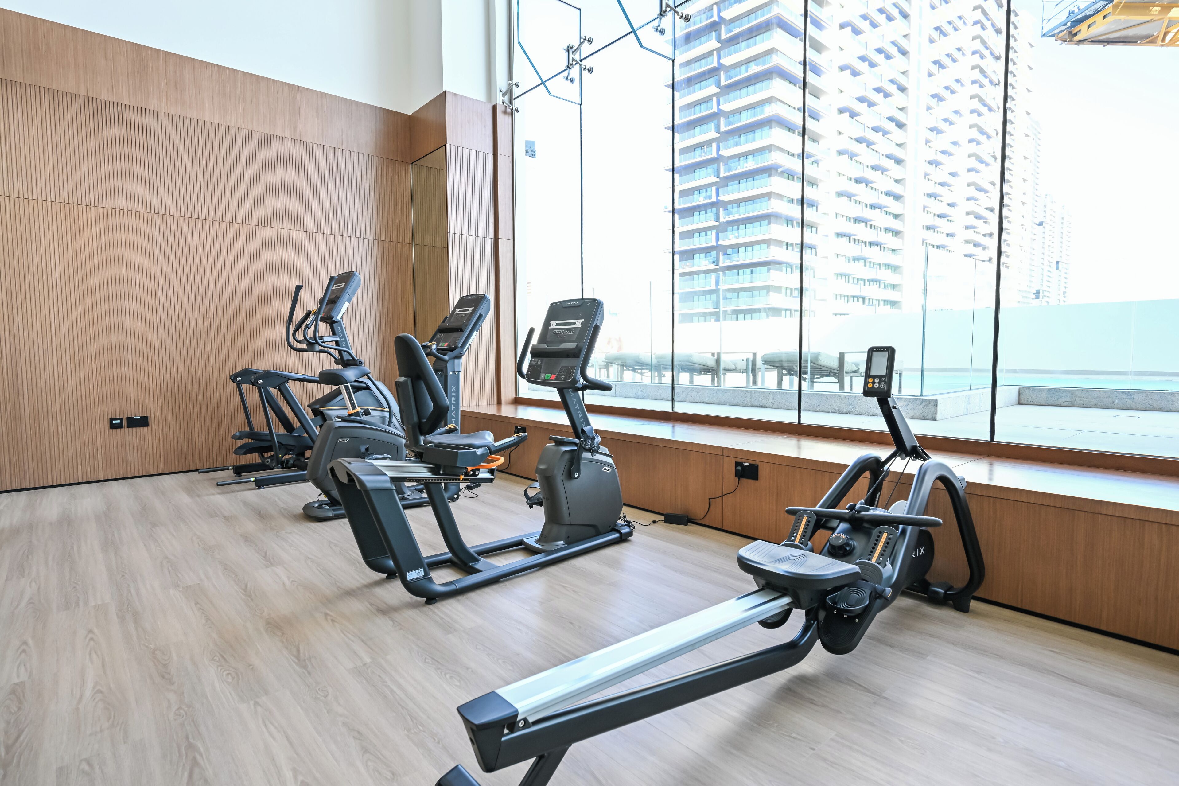 Een moderne sportschool met diverse fitnessapparaten, grote ramen en uitzicht op hoge gebouwen.
