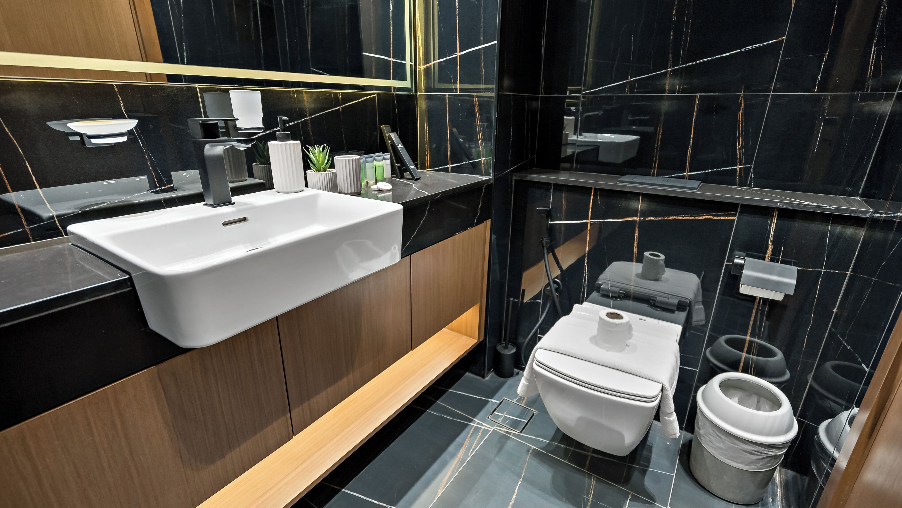 A modern bathroom with a white sink, black marble walls, and a wooden vanity.