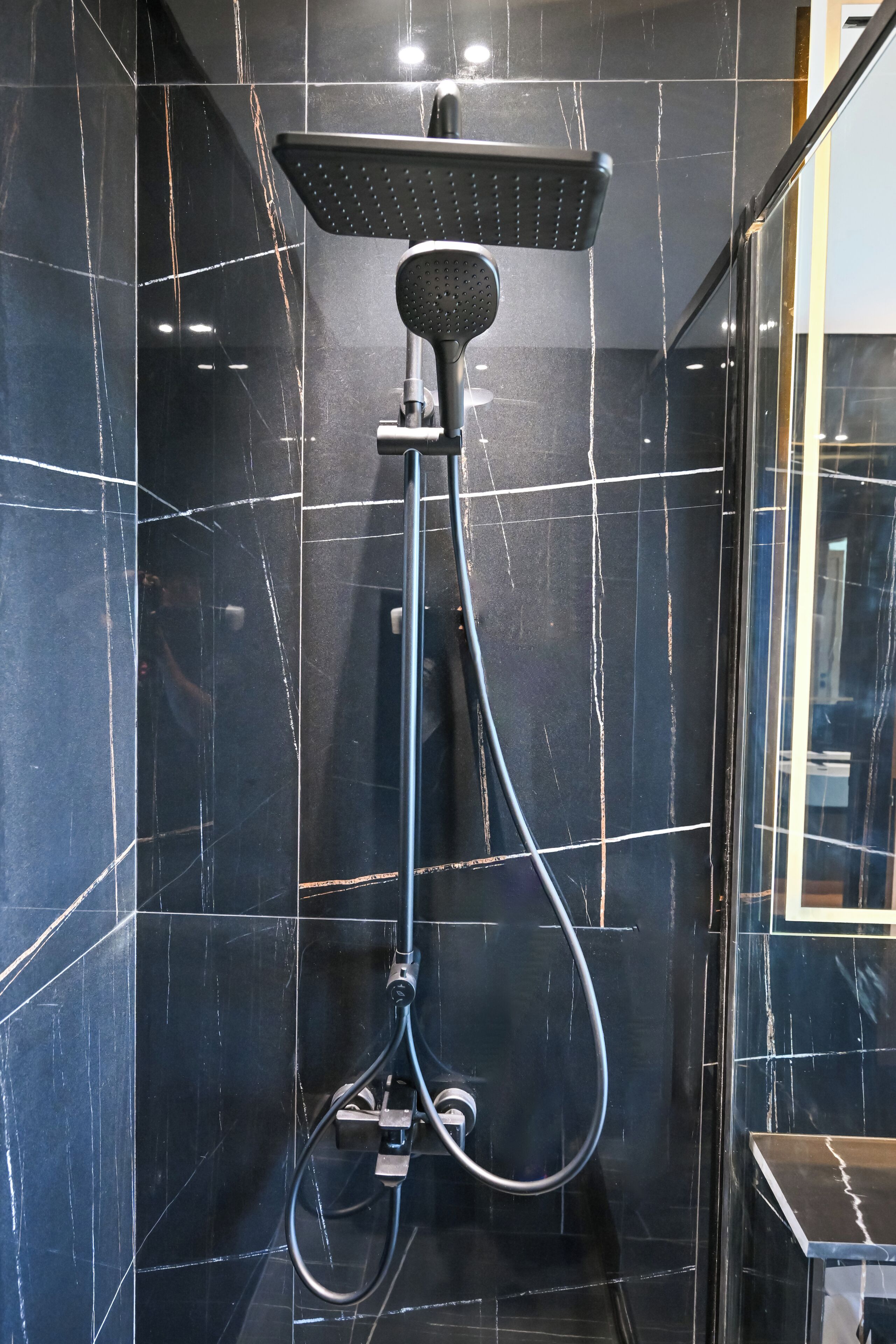 Une salle de bain moderne avec un espace de douche en marbre noir, une douchette à main et une zone de douche délimitée par des parois en verre.