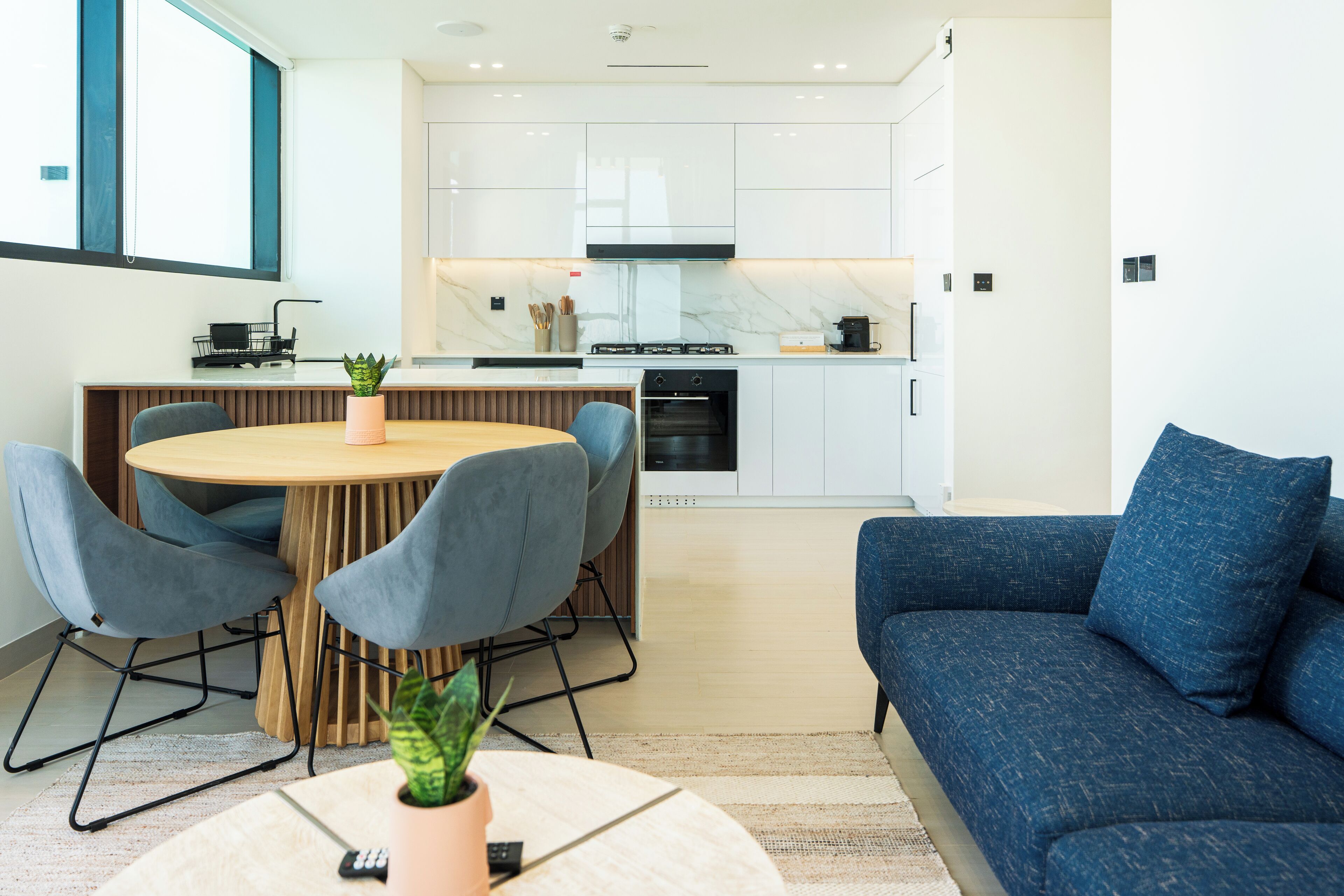 Een moderne keuken met witte kasten, een inbouwoven en een eethoek met een ronde tafel en stoelen.