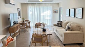 A modern living room with a sofa, dining table, chairs, and a TV. - Coral Beach #204 - by Zenbreak (Speightstown)