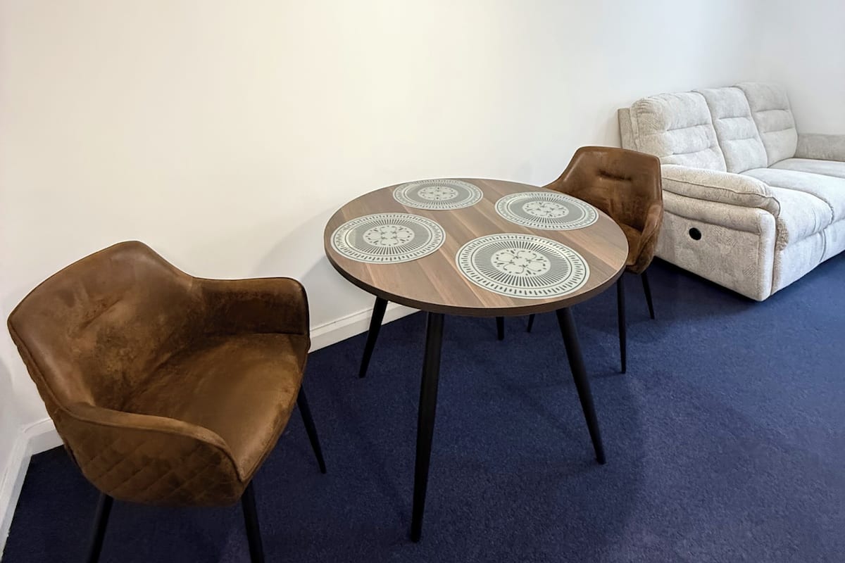 A room with a round table, two chairs, a sofa, and a ceiling light.