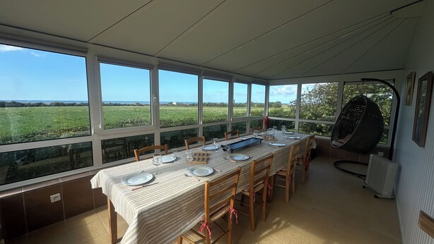 A dining area with a table set for four, large windows offering a view of a green field, and a hanging chair. - Sleeps 11, close to the sea (Tréogat)