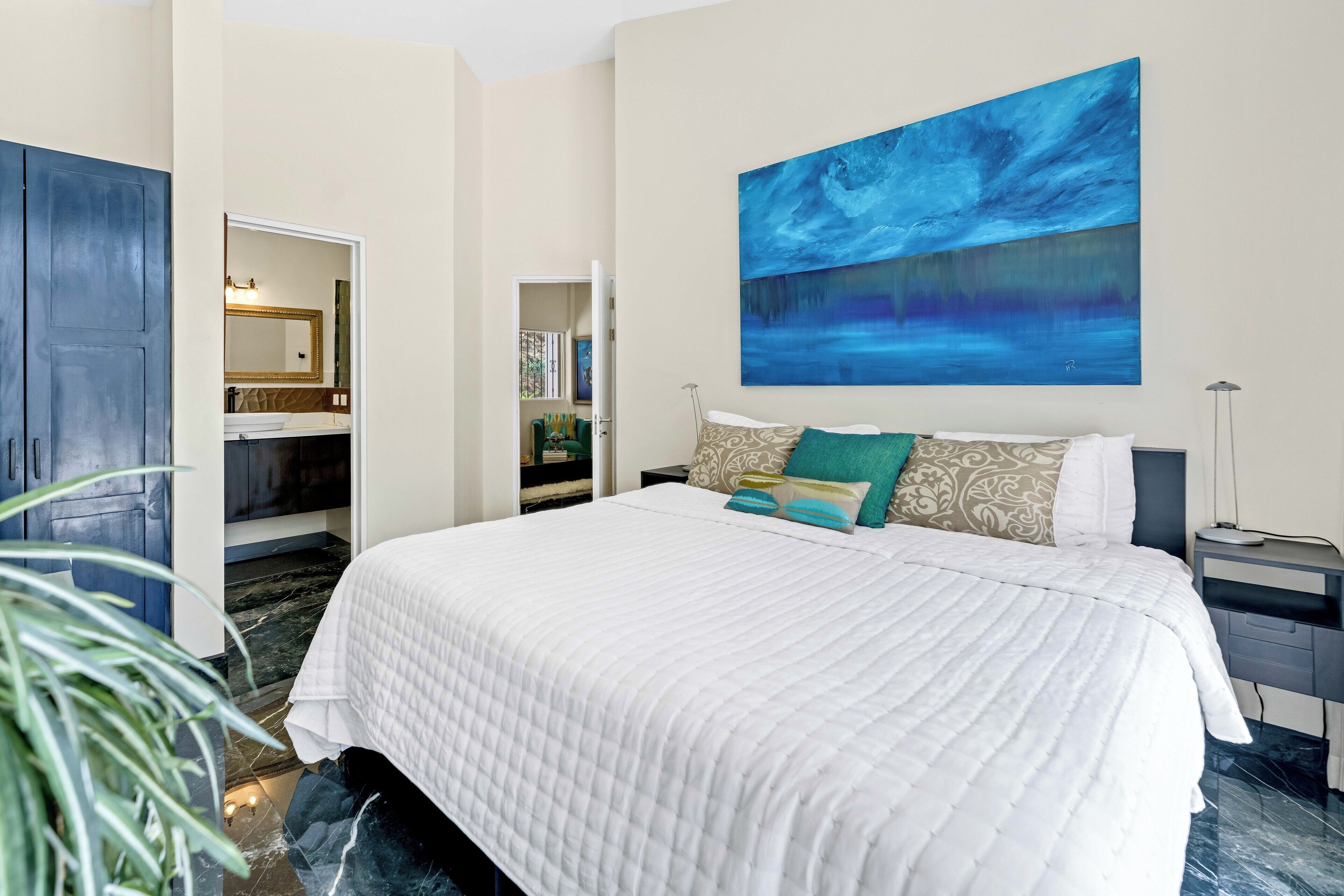 A bedroom with a large bed, a painting on the wall, and a wardrobe.