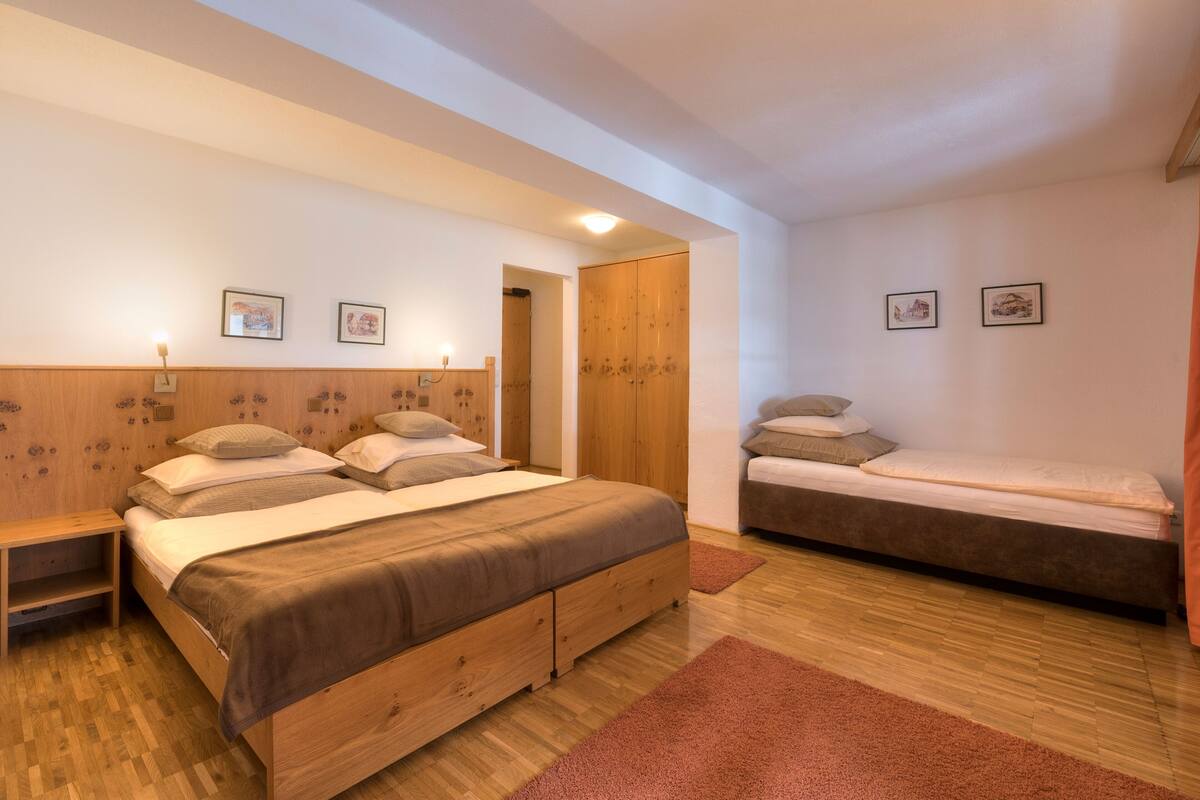 A bedroom with a large bed, a smaller bed, wooden flooring, and a wooden headboard.