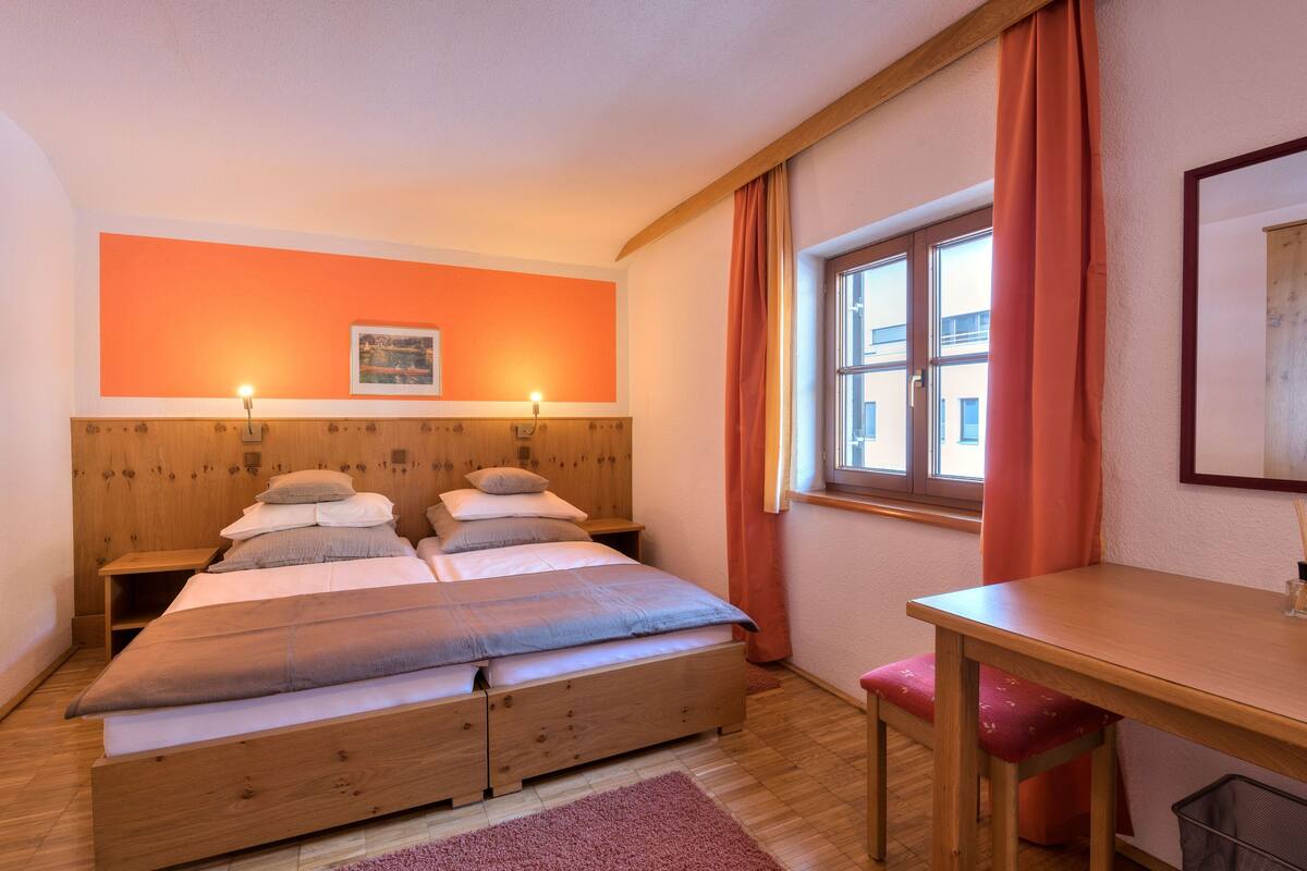 A bedroom with a wooden bed, two bedside tables, a desk, and a window with curtains.