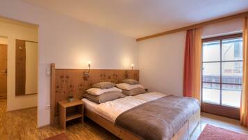 Une chambre à coucher avec un lit en bois, une table de chevet, un miroir et une fenêtre avec des rideaux.