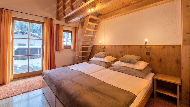 Un dormitorio con techo de madera, una escalera, una cama con almohadas y vistas a un edificio.