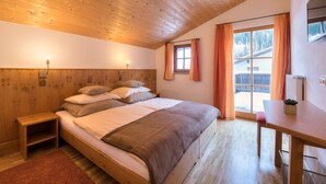 Un dormitorio con techo de madera, una cama con almohadas, una mesita de noche, una mesa y una ventana con cortinas.