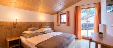 Un dormitorio con techo de madera, una cama con almohadas, una mesita de noche, una mesa y una ventana con cortinas.