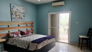 Une chambre à coucher comprenant un lit, une tête de lit en bois, un tableau, un climatiseur, une porte-fenêtre coulissante et une chaise.