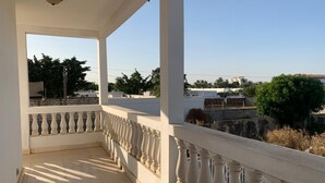 Un balcon avec une balustrade blanche, un ciel dégagé et des bâtiments qui se dessinent à l’horizon.