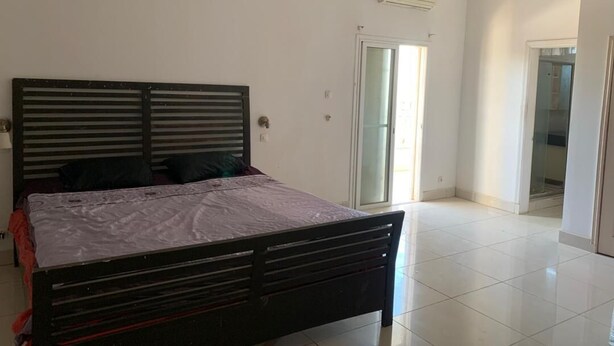 A bedroom with a bed, a sliding glass door, and a white tiled floor. - White house (Saly)