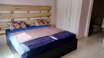 Ein Schlafzimmer mit hölzernem Kopfteil, einem Bett mit mehreren Decken, einem Kleiderschrank und einem angrenzenden Badezimmer mit Toilette.