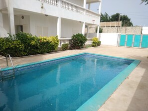 Une piscine rectangulaire dont le bord est recouvert de carreaux bleus, entourée d’une terrasse en béton.