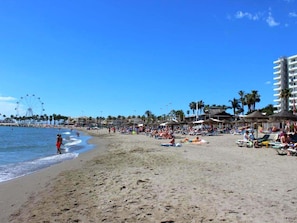 Una playa con noria, palmeras y sombrillas.