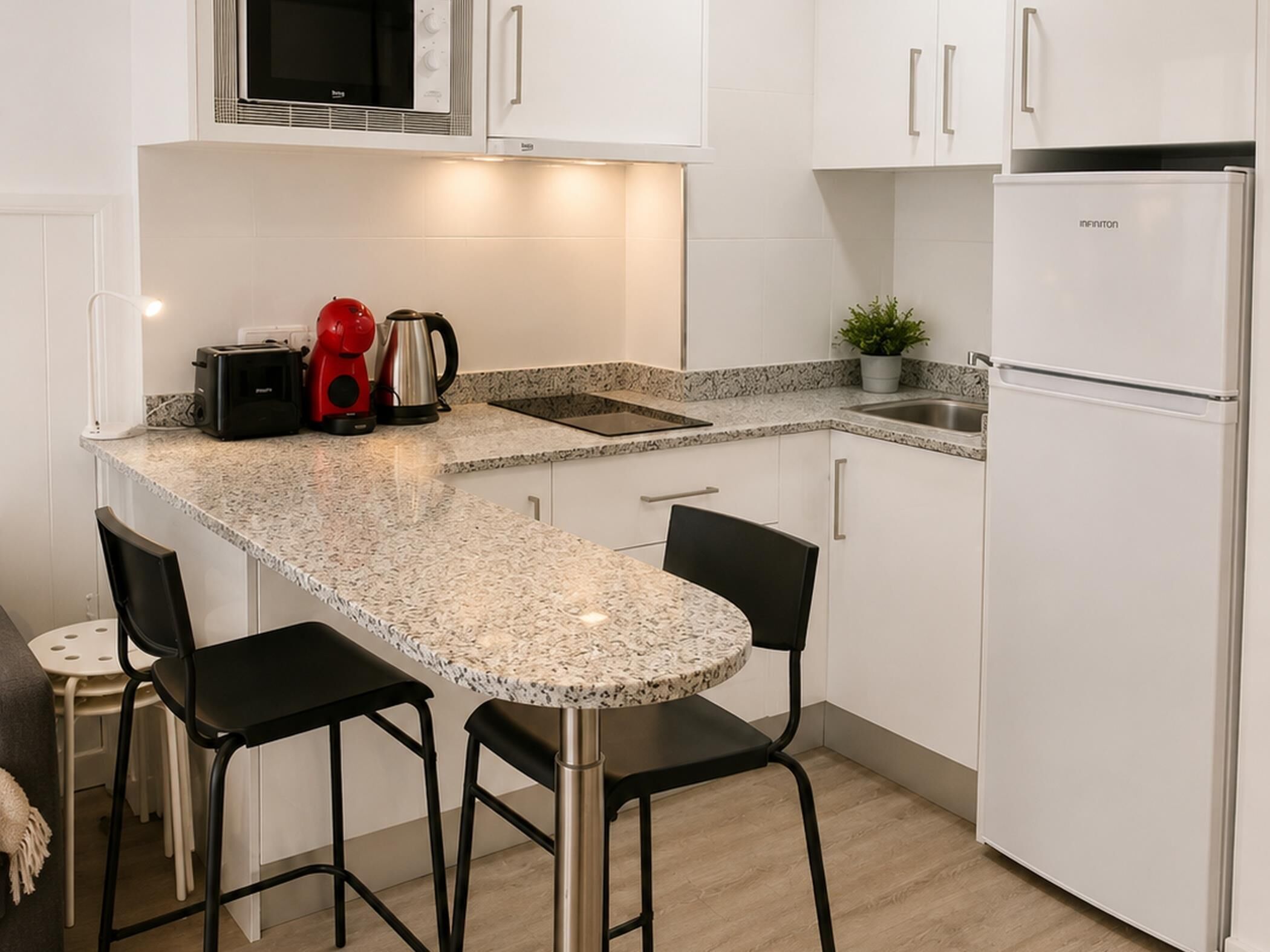 A kitchen with white cabinets, a granite countertop, a toaster, a kettle, and a refrigerator.