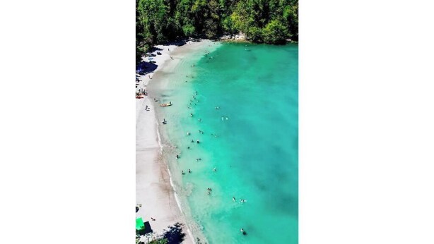 Vista aérea de una playa con aguas turquesas cristalinas y una orilla arenosa.