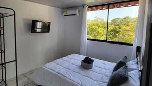Una habitación pequeña y limpia con cama, televisión y ventana con vistas a la vegetación.