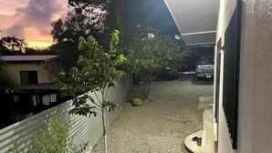 Un estrecho pasillo exterior con un sendero de grava, una planta en maceta y un coche aparcado.