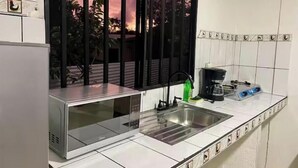 Una cocina con un lavamanos de acero inoxidable, una cafetera y una ventana con vistas a árboles y un atardecer.