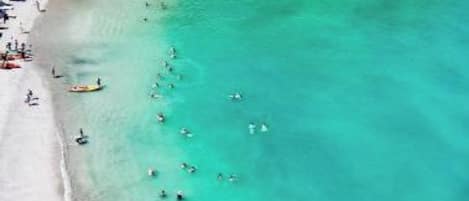 Une vue aérienne d’une plage aux eaux turquoise et limpides, bordée d’une végétation luxuriante.