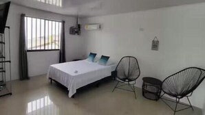 A bedroom with a bed, two chairs, a window, and a radiator.