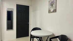 A room with a white door, a painting of a vase with flowers on the wall, and a round table with two chairs.