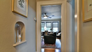 A hallway with a ceiling fan, a wooden floor, and a view into a living room with a dark-colored sofa and a patterned rug. - Historic Grove Park Rental - Apt #4 (Asheville)