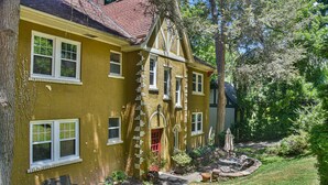 A yellow house with multiple windows, a red door, and a garden with a bench and potted plants. - Historic Grove Park Rental - Apt #4 (Asheville)