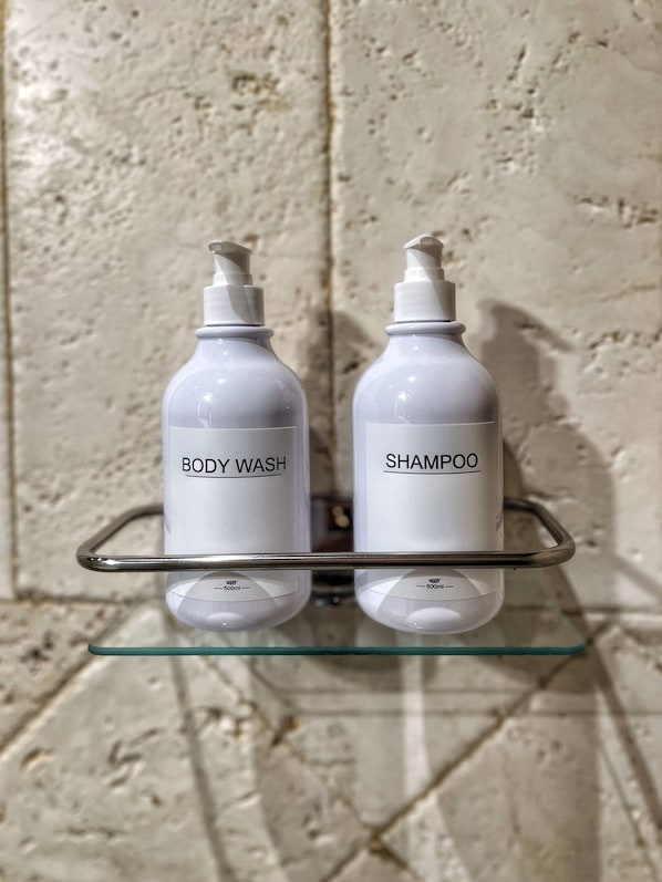 Two bottles of body wash and shampoo on a glass shelf against a textured wall.