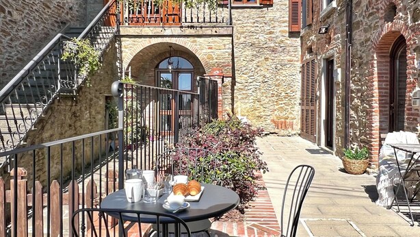 Un patio con edificios de piedra, mobiliario exterior y una escalera.