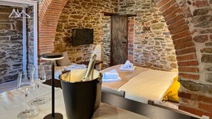 Una habitación acogedora con pared de piedra, cama, televisor y mesa con copas de vino.