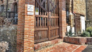 Un edificio de piedra tradicional con un porche de madera, una reja de metal y un camino de ladrillo que lleva a la puerta.
