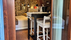 Una habitación acogedora con pared de piedra, una mesa de madera, una silla blanca y una cama con cabecera blanca.